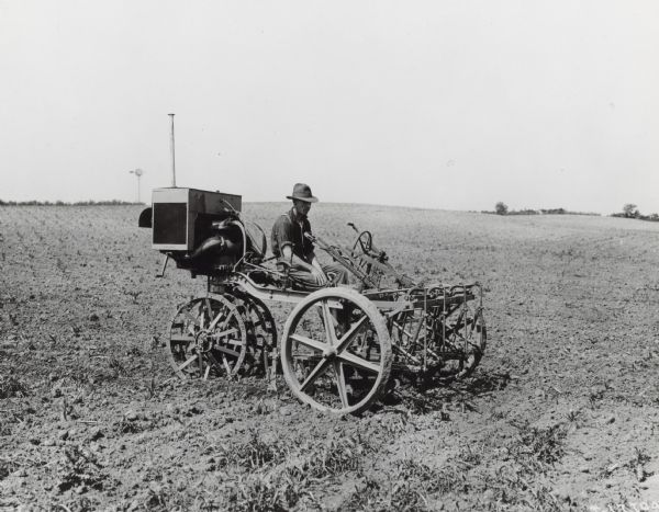 Three-quarter view toward front right of a man sitting on an International motor cultivator in a field.