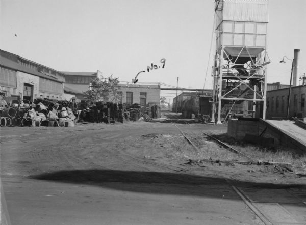 Exterior view of plant buildings. Writing on photograph reads: "No.9." Caption on front of photograph reads: "Yard — Looking East."