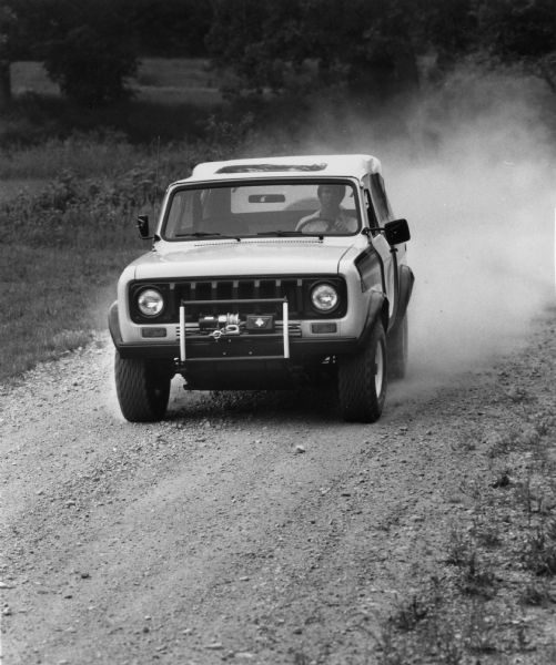 View towards a man driving a Scout SS-II up a road. News Photo sheet reads: "The 1979 International Scout SS-II is the Scout designed for four-wheel drive enthusiasts who want to tailor their vehicle to their own specific requirements. The SS-II has standard features including four-wheel drive, roll bar, and a fuel tank skid plate. It gives owners their option of passenger seating, a top and doors, and extra accessories."