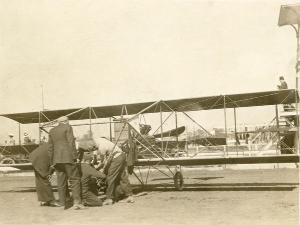 John Kaminski (who can barely be seen here in his Lincoln Beachey checkered cap), his mechanic, and onlookers attempting to ready his Curtiss pusher for flight.