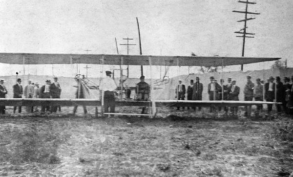 The 1911 Wright Model B rebuilt by Jesse Brabazon of Delavan and his partner-mechanic, Frank Shaffer. Brabazon, who is in the pilot's seat, is about to take off for the first time in the rebuilt plane.  He had purchased the wreckage from the family of Calbraith Perry Rodgers in the understanding that it was the <i>Vin Fiz</i>, the first plane to fly across the country and that the <i>Vin Fiz</i> was the plane in which Rodgers died in 1912. In fact, Rodgers' crash took place in his backup plane not the <i>Vin Fiz</i>. Mrs. Rodgers presented the actual <i>Vin Fiz</i> to the Carnegie Museum, which in turn presented it to the Smithsonian Institution where it is currently on display. However, the plane on display is hardly the plane built in the Wright Brothers' factory. Repairs on the cross country flight were so extensive that only two original parts were still in use when the <i>Vin Fiz</i> arrived in California.      

