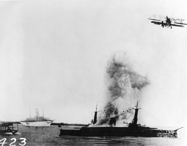 This photograph from the album of aviation pioneer Jesse Brabazon is described by him as the "first simulated bombing in history, using an aeroplane versus a warship." The print was presented to Brabazon by Lincoln Beachey. In the photograph it is Beachey who is dropping smoke bombs from his Curtiss pusher on to the Gorgonzola, a captured Spanish-American War battleship. In the background is the yacht Lyndonia.  Brabazon recalled that the source of Beachey's unsuccessful attempt to draw attention to the strategic potential of airplanes was a game of catch at Cicero Field between a pilot in an airplane and a man on the ground. This event predated the sinking of the Ostfriesland by several years.