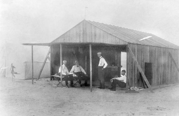 Wilbur Wright (standing, second from the right) with Edward C. Huffaker, Octave Chanute, and George Spratt in the workshed. Chanute was a special visitor from Chicago. At the turn of the century he was widely regarded as the elder statesman of aeronautical research. His 1894 volume, "Progress in Flying Machines," was the foundation for the Wright Brothers' work. At first a mentor for their experimentation, Chanute's role evolved to that of supporter.