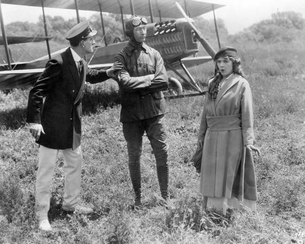 Donald Crisp, aviator Glenn Martin, and Mary Pickford in the 1915 silent comedy <i>A Girl of Yesterday</i> (Famous Players-Lasky, 1915). Martin is wearing a leather flying helmet, goggles, leather coat, and jodhpurs. Parked behind is a Martin Model TT biplane.