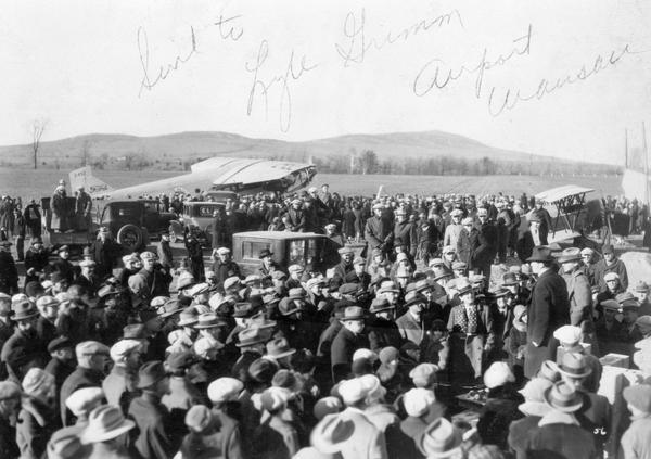 The groundbreaking ceremony for the new airport hangar at Wausau. Governor Fred R. Zimmerman, who can be seen on the right, (elevated above the crowd and wearing a dark coat and hat) had flown there for the ceremony in the Standard Oil Company plane parked in the background.
