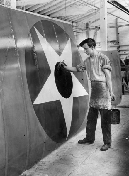 A factory worker painting the United States insignia on a bi-plane wing.