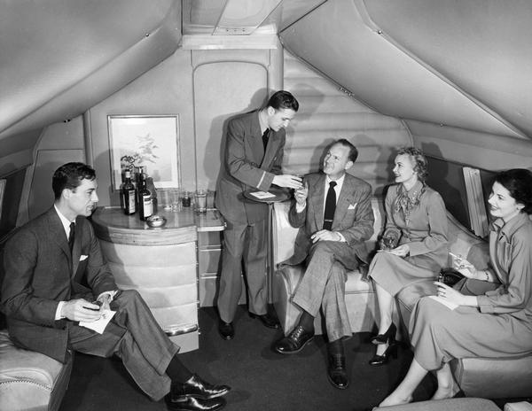 A steward serves four passengers in the bar and lounge of a TWA all-sleeper, trans-Atlantic Ambassador flight. The photograph is from the collection of company publicist Gordon Gilmore. Gilmore's papers are available for research at the Wisconsin Historical Society Archives.
