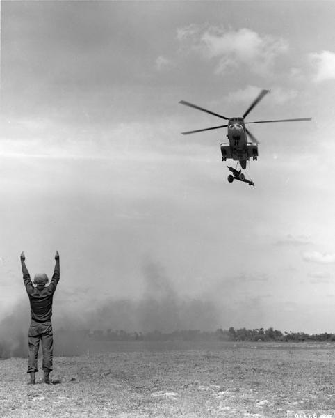 Arriving at a forward area, a U.S. Air Force CH-30 helicopter carrying a 105mm howitzer is directed in for a landing. The artillery piece, which was in a rear area and was needed by U.S., Vietnam, and Australian troops, was airlifted to the front in a matter of minutes.