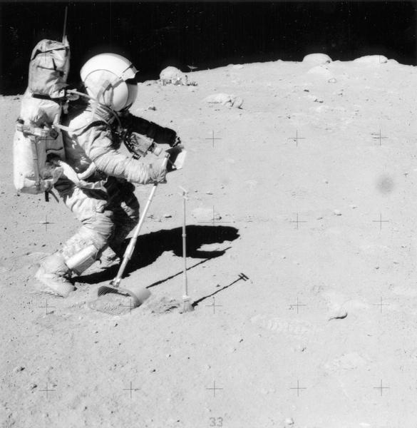 Astronaut Charles M Duke, Jr., collecting lunar samples using a rake and tongs. This photograph was taken on the moon by John W. Young, the crew commander. Duke is also wearing a chest-mounted 70mm Hasselblad camera. This photograph is part of a collection of NASA press information gathered by ABC News broadcaster, Jules Bergman.