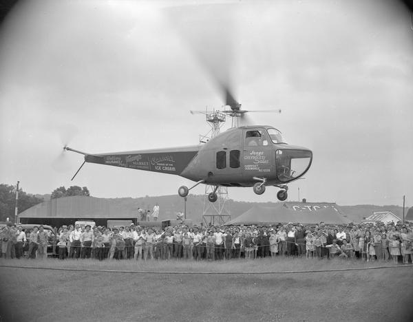 A helicopter hovers over the crowd at an air show marking the dedication of the Lone Rock Airport as a local government facility. Because of its location at the intersection of two mail routes, a tiny airport was established at Lone Rock during the 1920s. In 1954 the Civil Aeronautics Administration relinquished control and operations were taken over by Sauk, Richland, and Iowa counties.