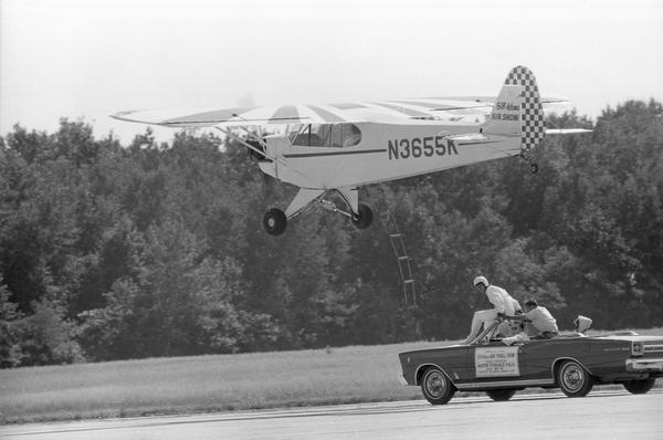 The Bill Adams company prepares to perform ground-to-plane transfer with a clipped-wing Piper Cub at Austin Straubel Airport.
