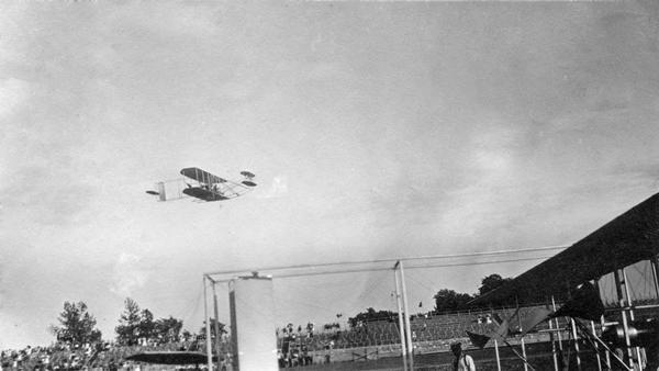 A Wright airplane flying over a grandstand in Indianapolis, with a second unidentified plane in the foreground. This exhibition at the recently-constructed Indianapolis Speedway was organized by the Wright Brothers in order to increase sales. All of the flying was done by members of their exhibition team. This snapshot was taken by Arthur Pratt Warner, Wisconsin's first aviator, who attended several aviation exhibitions during 1910.
