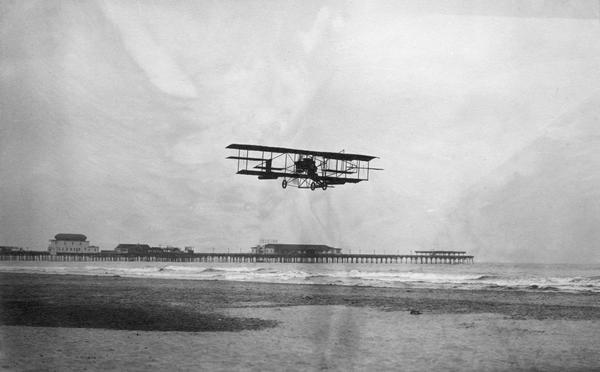 Glenn Curtiss flying over the ocean. The pontoons under each wing illustrate the beginnings of his development of amphibious aircraft. The famous Steel Pier is in the background.