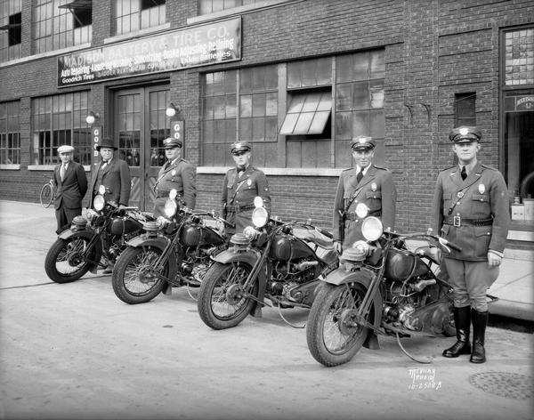 Four Dane County motor police officers shown with four Harley Davidson motorcycles, and two other men, taken in front of Madison Battery and Tire, 250 State Street.