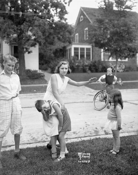 Virginia Gillette demonstrates how residents in the 400 block of Virginia Terrace are combating traffic dangers by spanking. Dicky Dupois is over her knee, while Joan Duffee, Woodrow Wheeler, and a boy on a bicycle observe.
