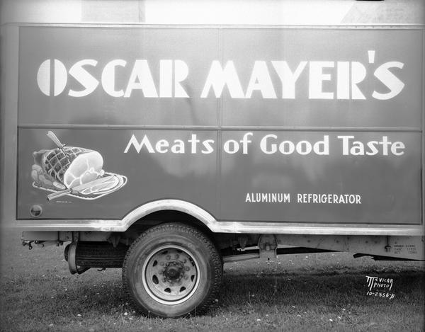 View of side of truck parked outdoors in the grass, with the words: "Oscar Mayer's Meats of Good Taste. Aluminum Refrigerator."