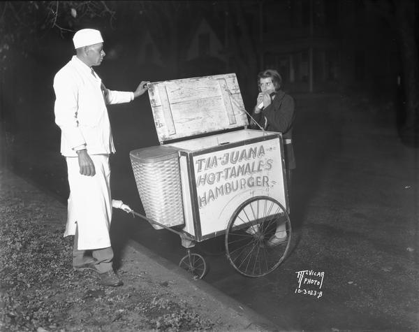 William Pearl with his "Tia Juana hot tamales" cart and a woman customer eating a hot tamale.