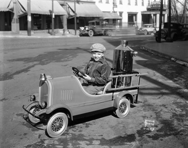 Myron Praga on toy fire engine run by a 1/2 horsepower motor and a 6 volt storage battery housed in the tank. He is parked at the corner of King and Doty Streets. The vehicle was built by J.P. Reed from a pedal car.