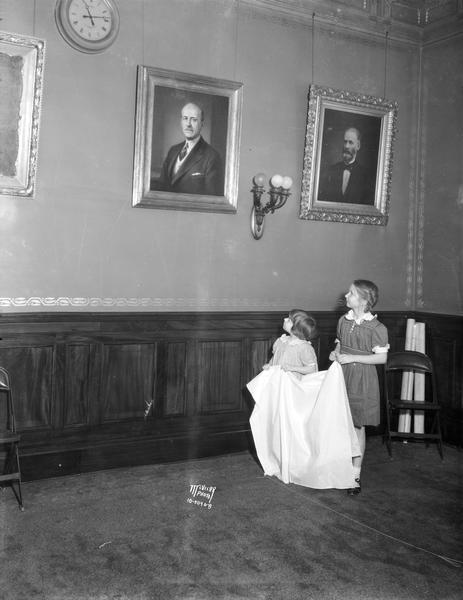 Portrait of Governor Albert G. Schmedeman, painted by Merton Grenhagen, in the gallery of governors at the Wisconsin State Capitol. Mary and Shurley, daughters of Mr. and Mrs. Leonard Von Spach, Wauwatosa, are pulling the cord for the unveiling. At the right is the portrait of former Governor William Smith.