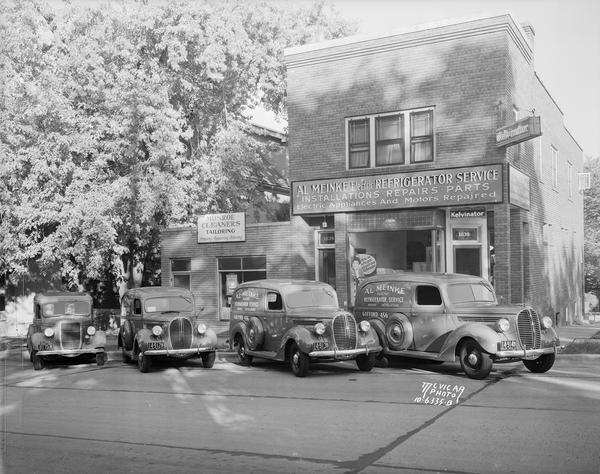 Three Ford V8 panel trucks and one automobile parked in front of Al Meinke Electric Refrigerator Service store, 1639 Monroe Sreet. On the left is Monroe Cleaners, 1637 Monroe Street.