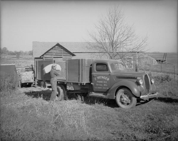 A man is loading a sack onto a Ford farm truck. The name on the truck door is F. Wenger, Verona, Wis.