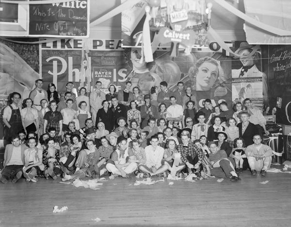 Acacia fraternity "Bowery" party, with couples in costume. There are many commercial posters and advertising on the wall in the background.