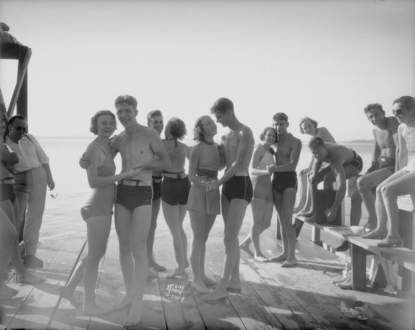 Group of men and women modeling bathing suits that have been approved by the police chief on the Alpha Chi Omega pier on Lake Mendota.