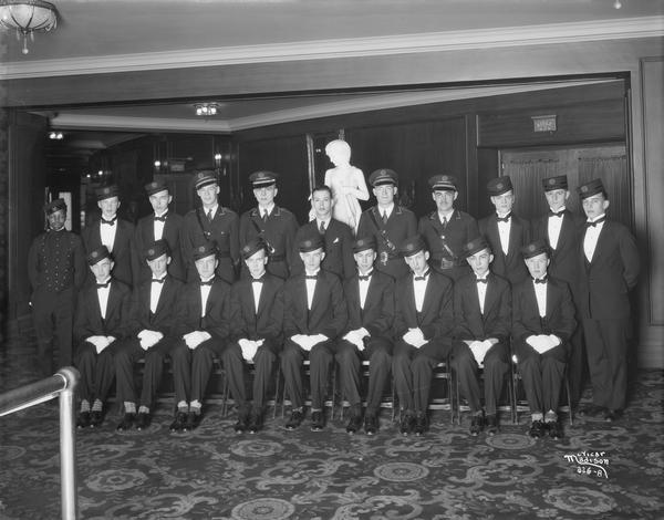 Group portrait of new Orpheum Theatre ushers. Behind the group is a statue of a boy with a goat on a pedestal near the "Aisle 2" doors to the auditorium.