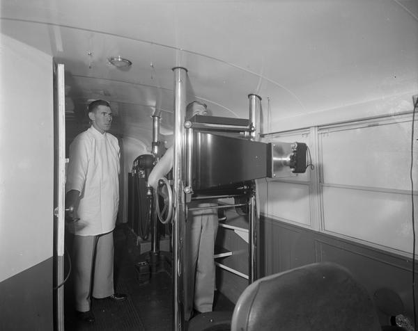 School bus interior with a mobile x-ray machine. A male technician stands by while another man stands in front of the diagnostic unit.