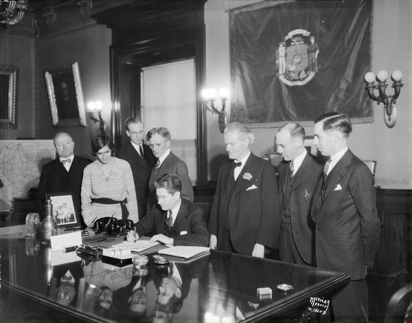 Governor Philip F. La Follette signing unemployment insurance law.  Left to right: Henry Ohl Jr., Mrs. Elizabeth Brandeis-Raushenbusch, Paul Raushenbusch, Professor John R. Commons, Lieutenant Governor Henry A. Huber, Assemblyman Harold M. Groves, Assemblyman Robert A. Nixon.