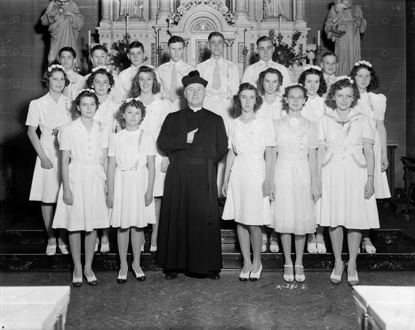 Group portrait of St. Patrick's eighth grade graduation class, with a priest in front of the altar, 410 East Main Street.