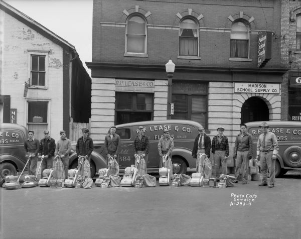 R.F. Lease and Co., 209 East Main Street, company truck, with eleven men standing beside their floor sanders. Other business in view, Madison School Supply, 207 East Main Street.