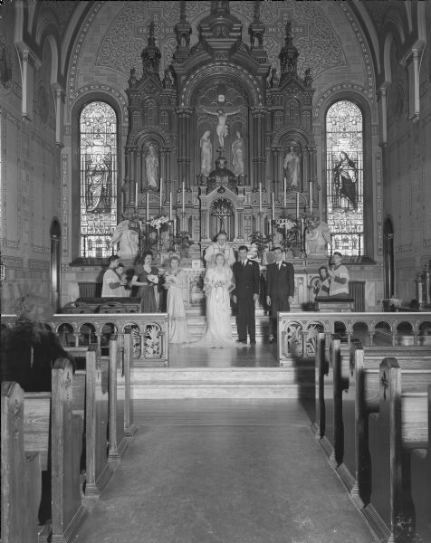 Wedding party at the altar of Sacred Hearts Catholic Church. Party includes bride Marian Thekla Hebl, groom James Daniel Tormey, Priest George Haeusler, bridesmaids Arlene Hebl and Iona Miller, best man John Tormey and four altar boys.