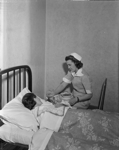 Nurse Alma Padgett feeding a patient from a tray of food at Mendota State Hospital (Mendota Mental Health Institute).    