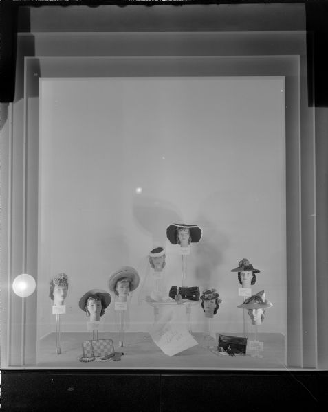 Display of eight fancy women's Easter hats in Manchester's, Inc., store window.