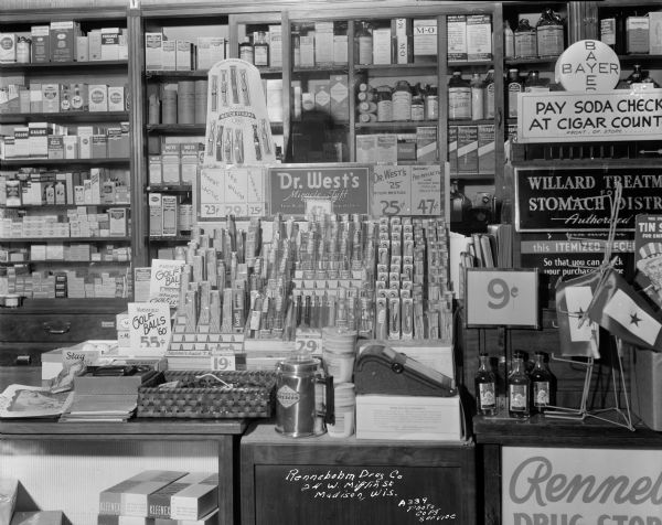 Counter display of Dr. West's Miracle Tuft toothbrushes at Rennebohm Drug Store, 24 West Mifflin Street. A sign advises customers to "Pay Soda Check at Cigar Counter."