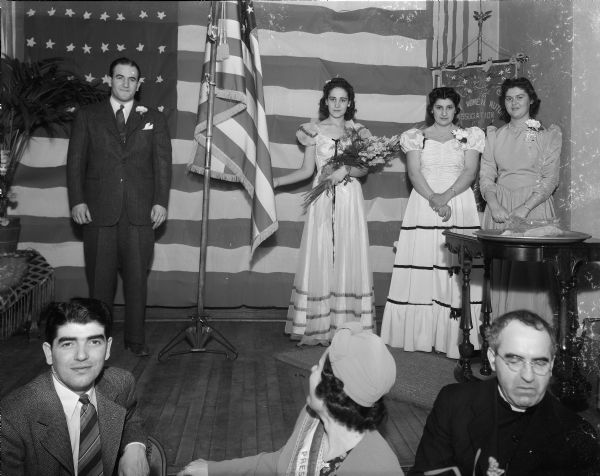 Phillip Canepa with Virginia Licari, Marian Amato and Josephine (Florence ?) Clementi on the platform dedicating a United States flag at the Italian Workingmen's Club House, 914 Regent Street, Greenbush.  Looking on are Joseph "Jobo" Puccio and his wife Edna "Tootsie" Mazzara Puccio along with Father Julius Neault, pastor at St. Joseph's Catholic Church.  Taken on the occasion of the Italian Women's Mutual Society 7th anniversary banquet.
