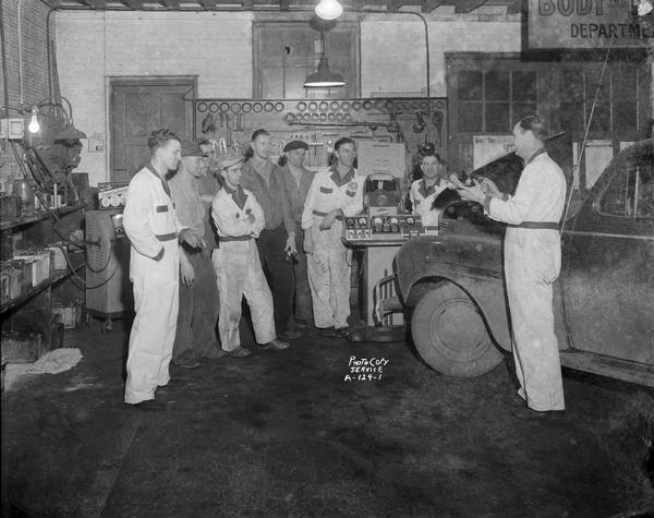 Mechanic demonstrating products to a group of mechanics in the work shop, Schultz Tire and Battery Service, 1336 Regent Street.