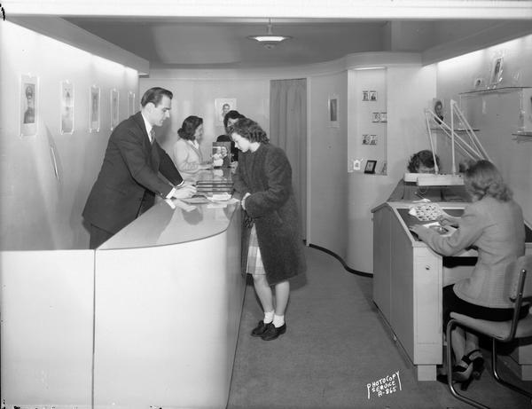 The photo studio department in Manchester's Department Store. A man is assisting a female customer, while female employees do their work.