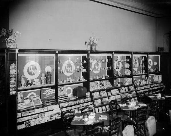 Union News Company merchandise display cases along the wall at Chicago & Northwestern Depot, 219 S. Blair Street. The display features gifts, magazines, and postcards. There are also three snack tables and chairs in front of the display cases.