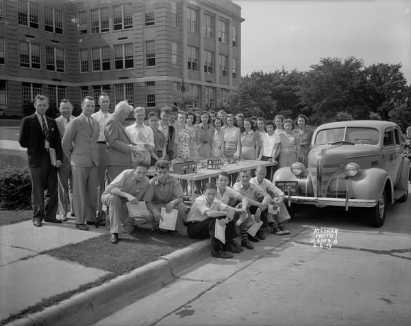 Group of students in the new drivers class stand in front of West High School with a new automobile and a scale model of Madison's streets. Includes five adults. Taken for American Automobile Association.