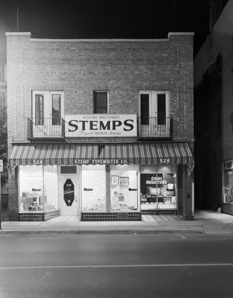 Stemp Typewriter Company, located at 528 State Street, featuring the entire front view of the building, including sign "Stemps Adding Machines, expert repair service," four show windows with display of equipment and sign that reads: "Cash Registers."
