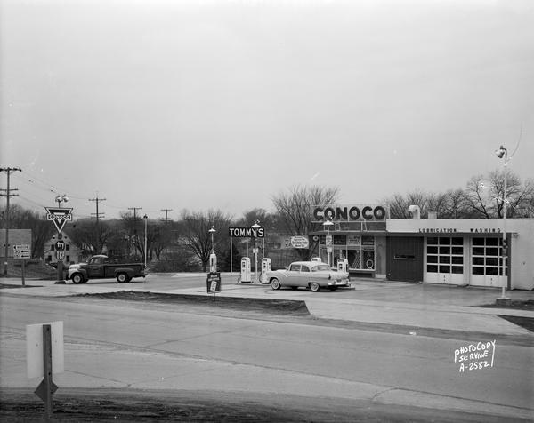 Exterior of Tommy's Conoco Oil Station, 3116 East Washington Avenue at Commercial Avenue (aka Highway 30). Includes gas pumps, one automobile, and a Tommy's truck. Run by William K. Thomas.