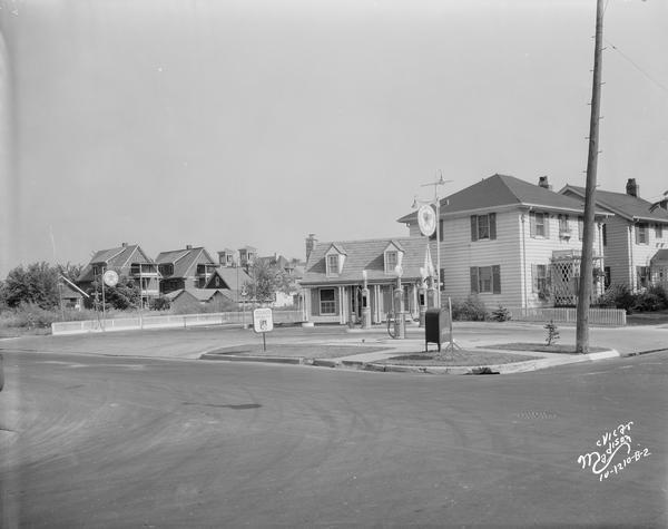 View of Texaco service station, 1337 Regent Street at Randall Avenue, with the towers of St. James Catholic Church in the background behind buildings.