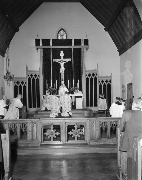 Father Paul N. Flad faces the congregation during his first Mass at Blessed Sacrament Church, 2119 Rowley Avenue, with priests and altar boys kneeling in prayer.