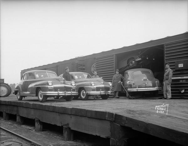 Four men posing with the first shipment of new 1946 DeSoto automobiles as they come off a train onto a loading dock for Stadium Garage, 1501 Monroe Street, Plymouth and DeSoto Sales and Service.