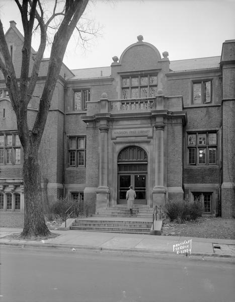 View from street towards a man approaching the entrance to the Madison Free Library, 206 North Carroll Street. The library was built with Carnegie money and opened in 1906. The name changed to Madison Public Library in January 1959. 
 This building was torn down in 1965 when the library moved to a new building at 201 West Mifflin Street.