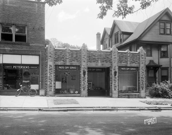 Exterior view of the Photo Copy Service building at 211 West Mifflin Street, next to Pettersen's carpets and linoleum, 209 West Mifflin Street. Also shown is an apartment house at 215 West Mifflin Street.