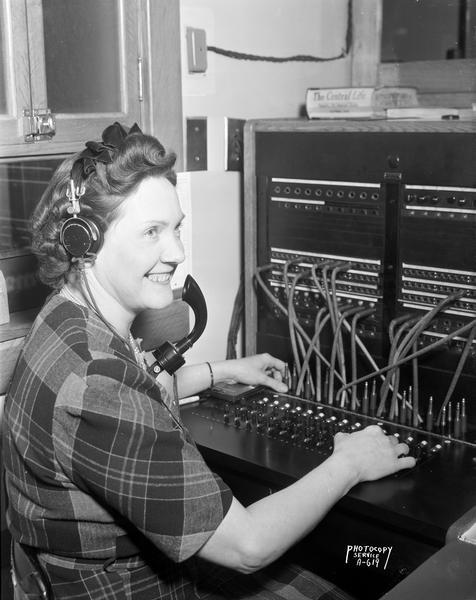 A telephone operator wearing a headset sits in front of a switchboard at the Oscar Mayer Co.
