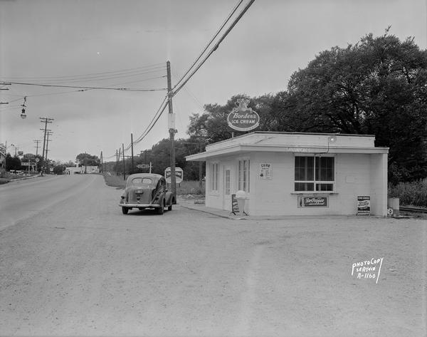 An automobile parked in front of the West Side Fountain operated by John P. Stein and Joseph Scalissi with Borden's Ice Cream, Dr. Pepper, Pepsi and Royal Crown signs, on Middleton Road (2900 block of University Avenue), just before the entry to the Post Farm.  Farther out is Lester Dingledine's Mobile Service Station.  On the other side of the road there was a tourist cabin business run by Walter and Bertha Sullivan and James Fush's Texaco Service Station. Photograph taken for Kennedy-Mansfield Dairy Company.